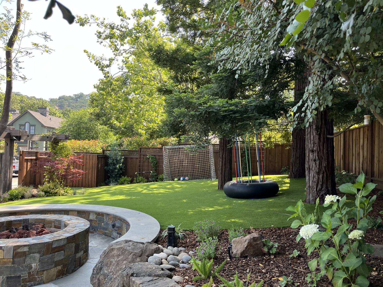Twin Palms Landscape artificial turf lawn, planting beds, and stone fire pit in a Bay Area backyard