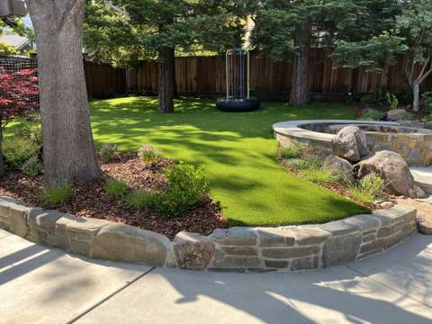 Artificial turf lawn bordered by curved stone curbing and mature trees