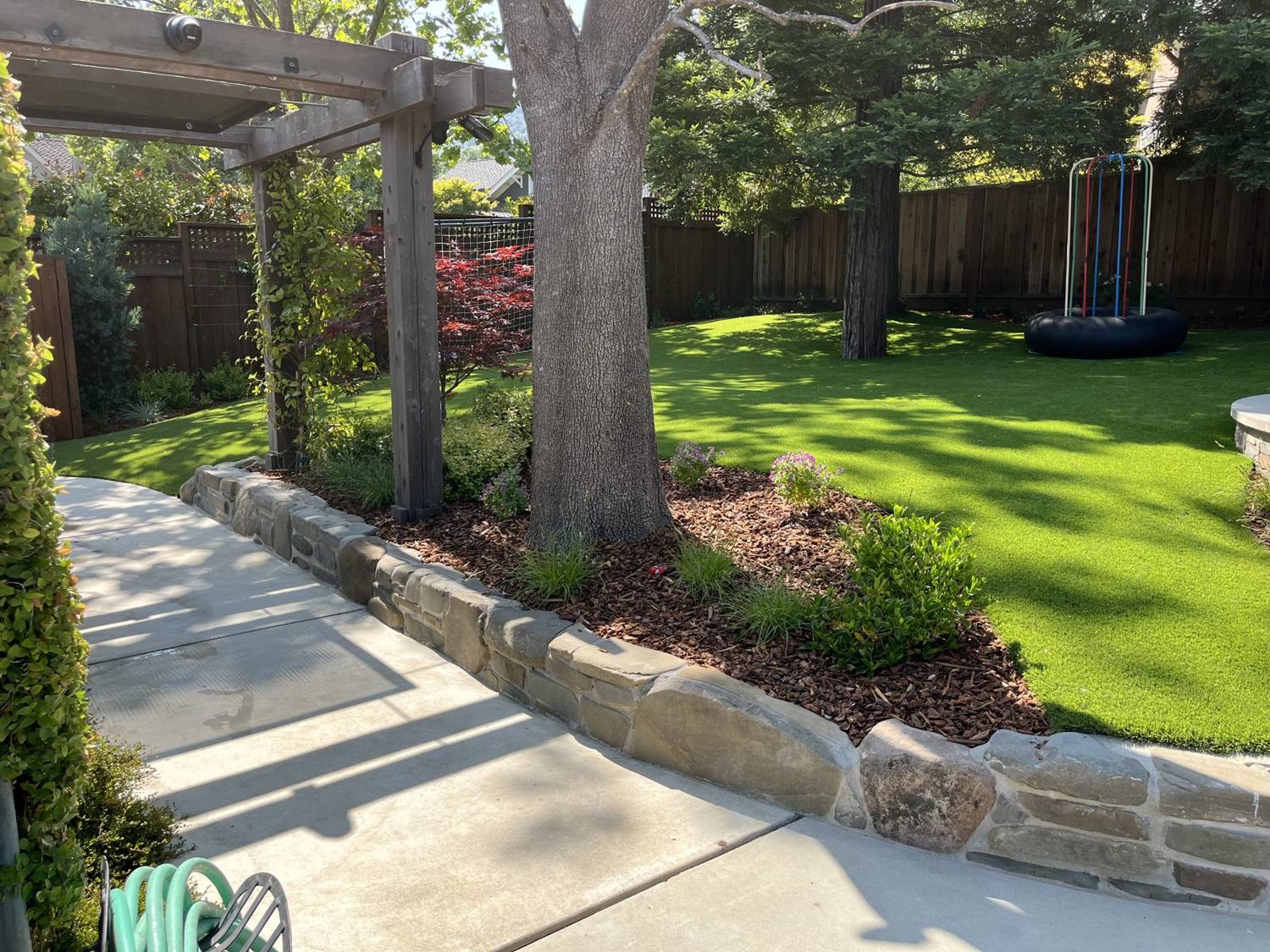 Artificial turf lawn with stone curbing and pergola in a backyard